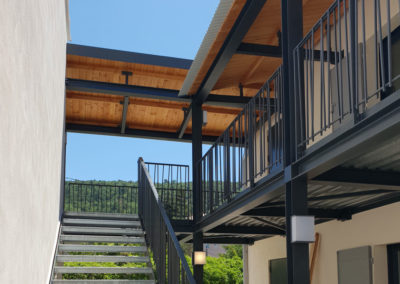 Passerelle extérieure avec garde corps à barreaux acier croisés et auvent métal et bois