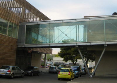 Passerelle extérieure couverte en verre et métal posée sur poteaux